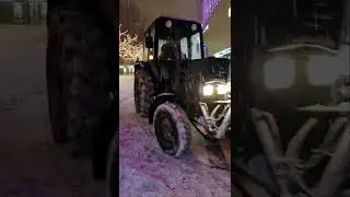 Синий трактор сыпет соль на дорогу из бункера среди гирлянд. МТЗ с разбрасывателем соли.