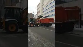 Трактор загружает снег в грузовик-самосвал.