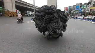 Hundreds of tyres are balanced on motorbike as it drives down road in Vietnam